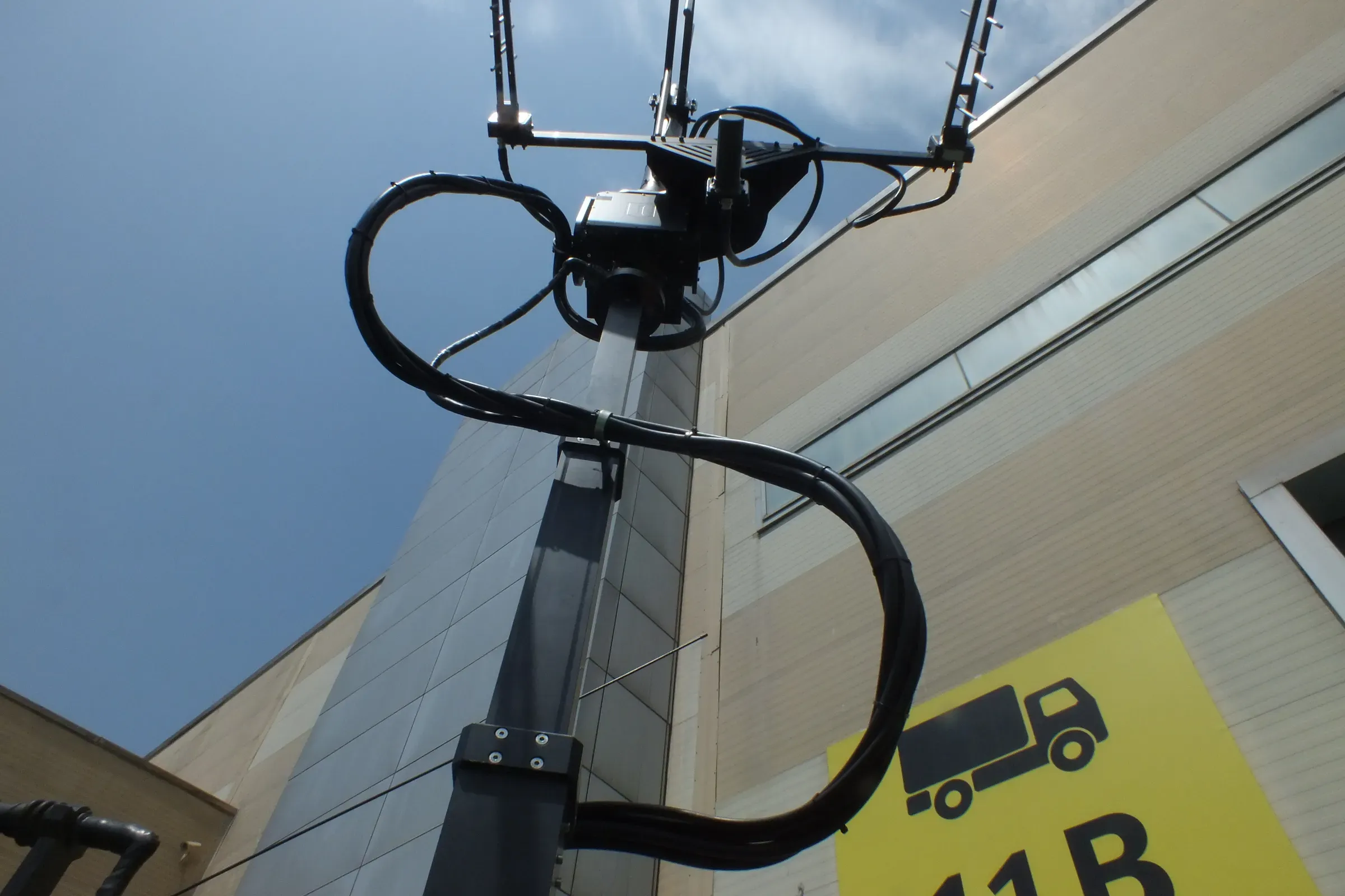 Close view of mast head with looped cable and guy arms against sky, hall sign behind.