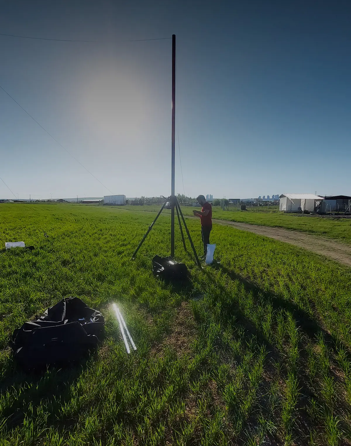 Portable mast deployed at full height in open country, with transport cases beside it