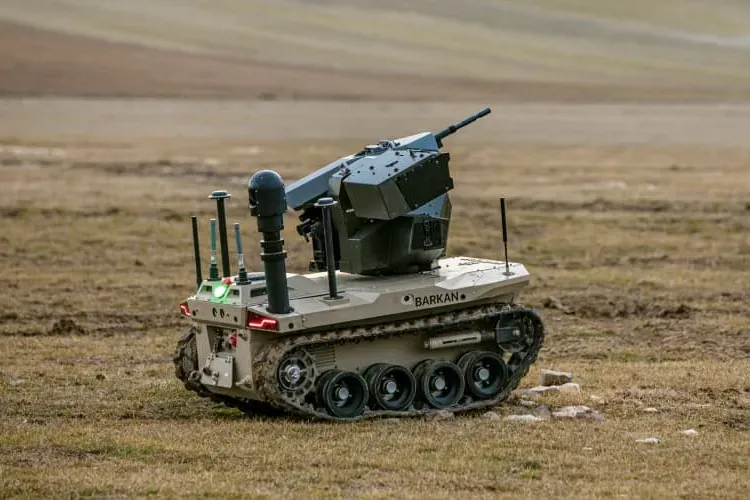 Tan tracked vehicle with turret and extended mast on a grassy hillside, blurred rolling fields behind.