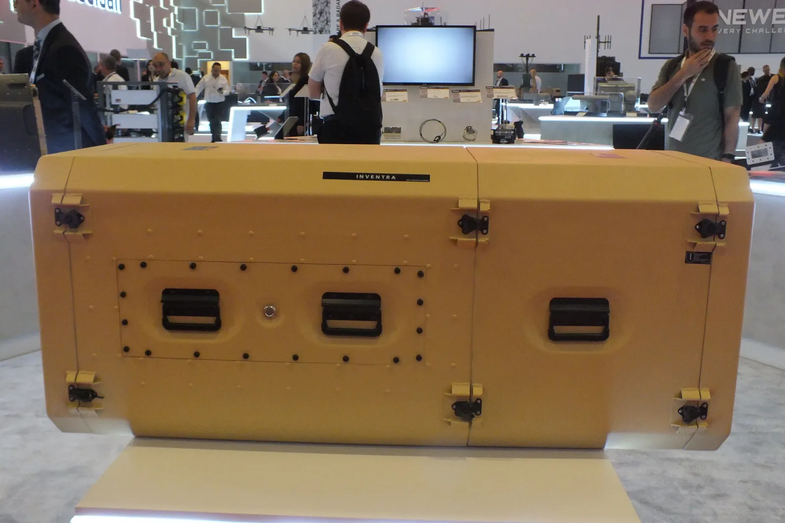 Sand-coloured transportable rack cabin on the exhibition stand, its latches and side handles visible.