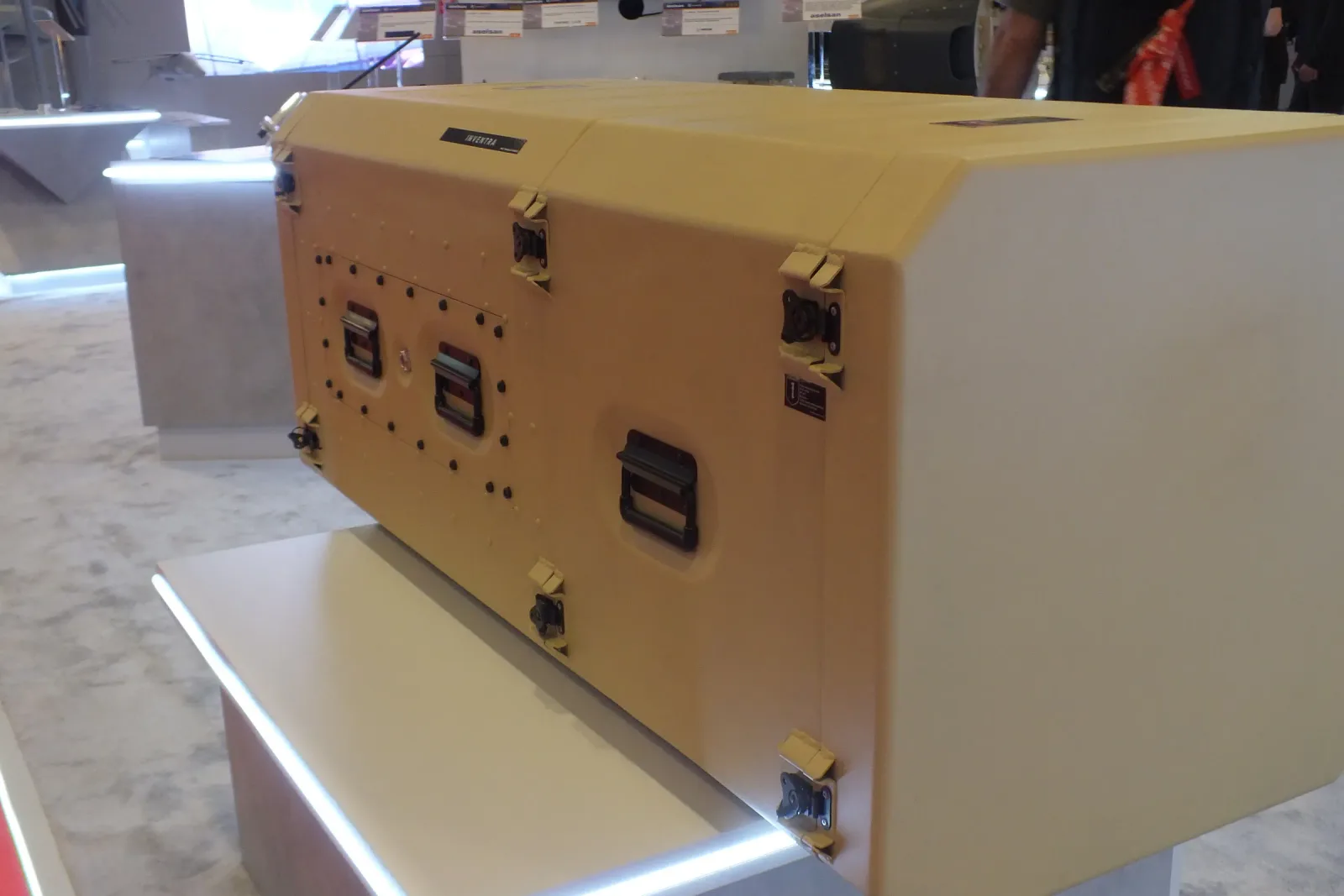 Sand-coloured transportable rack cabin on the exhibition stand, its latches and side handles visible.
