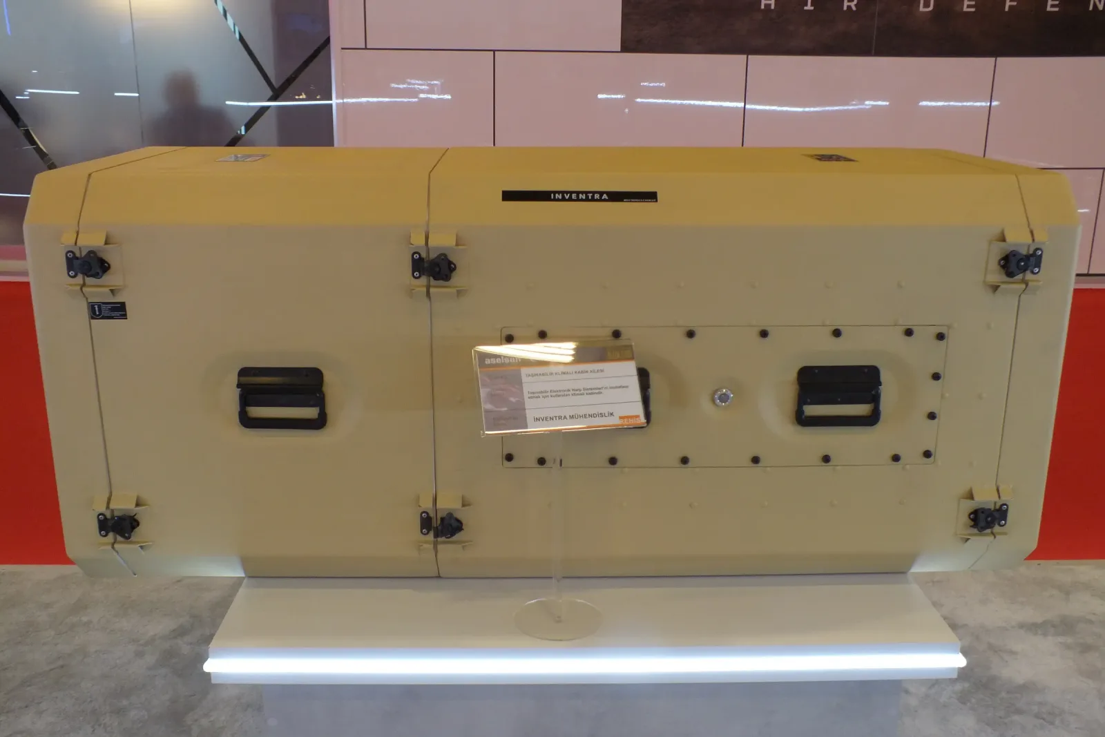 Sand-coloured transportable rack cabin on the exhibition stand, its latches and side handles visible.