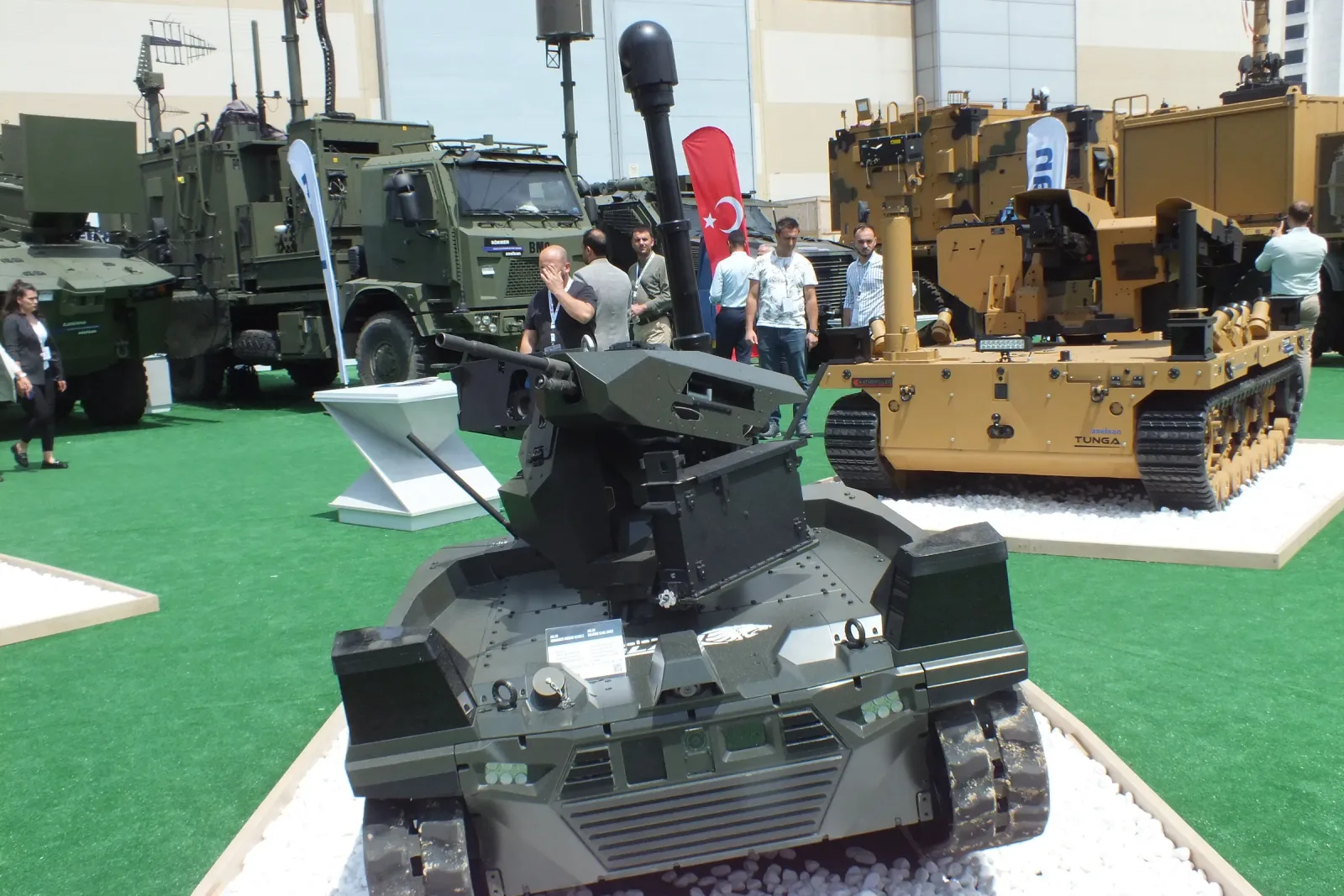 A tracked unmanned ground vehicle on the stand with a telescopic mast raised and a stabilised gimbal at its top.