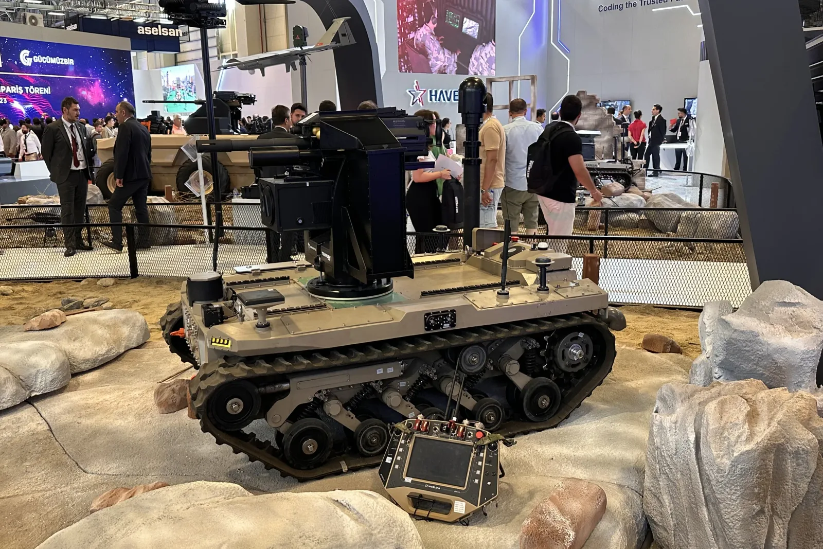 A tracked unmanned ground vehicle on the stand with a telescopic mast raised and a stabilised gimbal at its top.