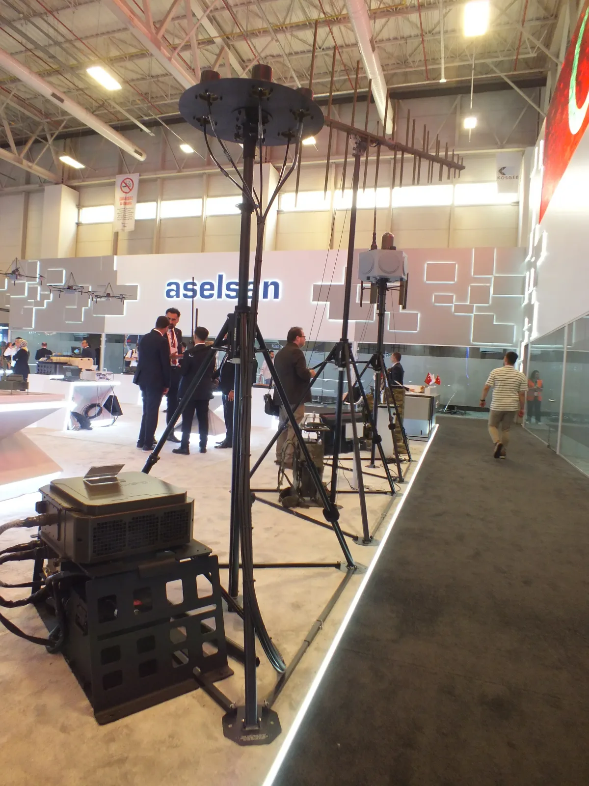 A portable tripod mast set up on the exhibition floor with its guy rings and payload head.