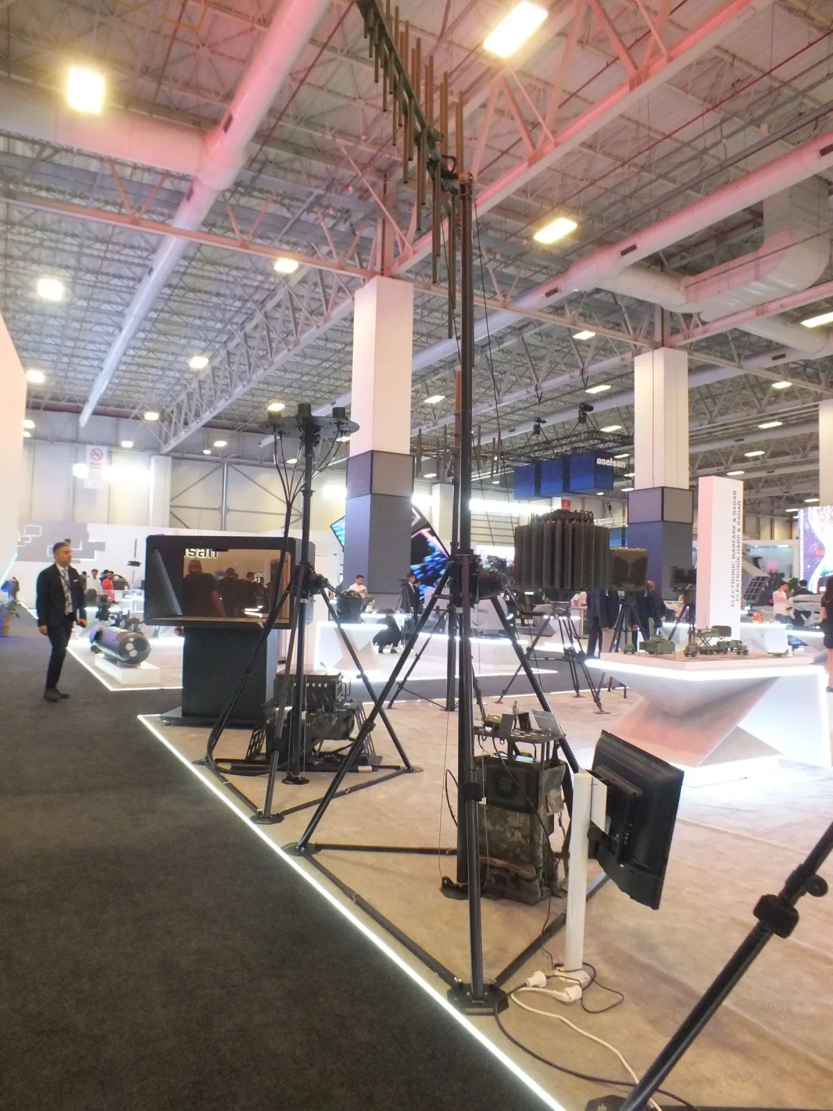 A portable tripod mast set up on the exhibition floor with its guy rings and payload head.