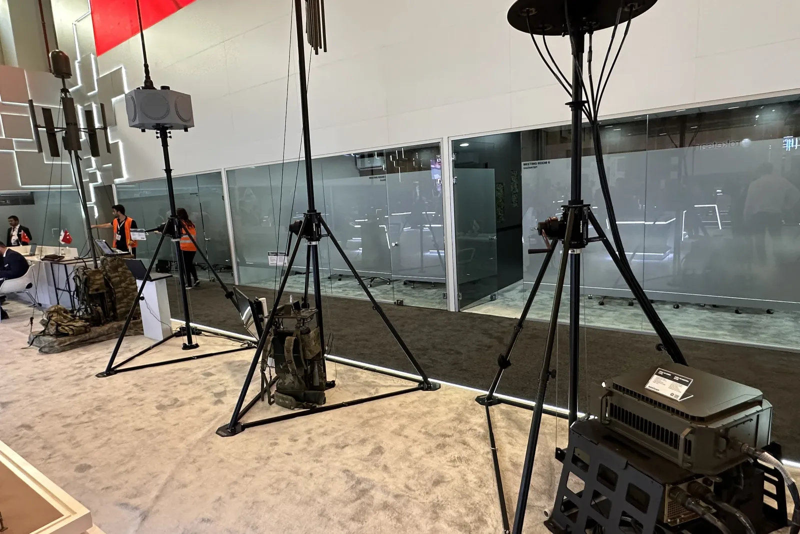 A portable tripod mast set up on the exhibition floor with its guy rings and payload head.