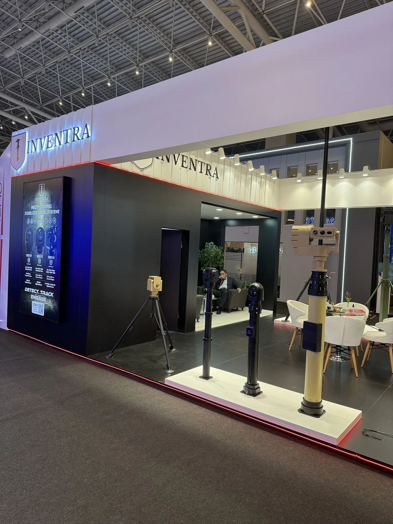 Side of the stand: tripods and masts along the white platform, the gimbal banner on the end wall.