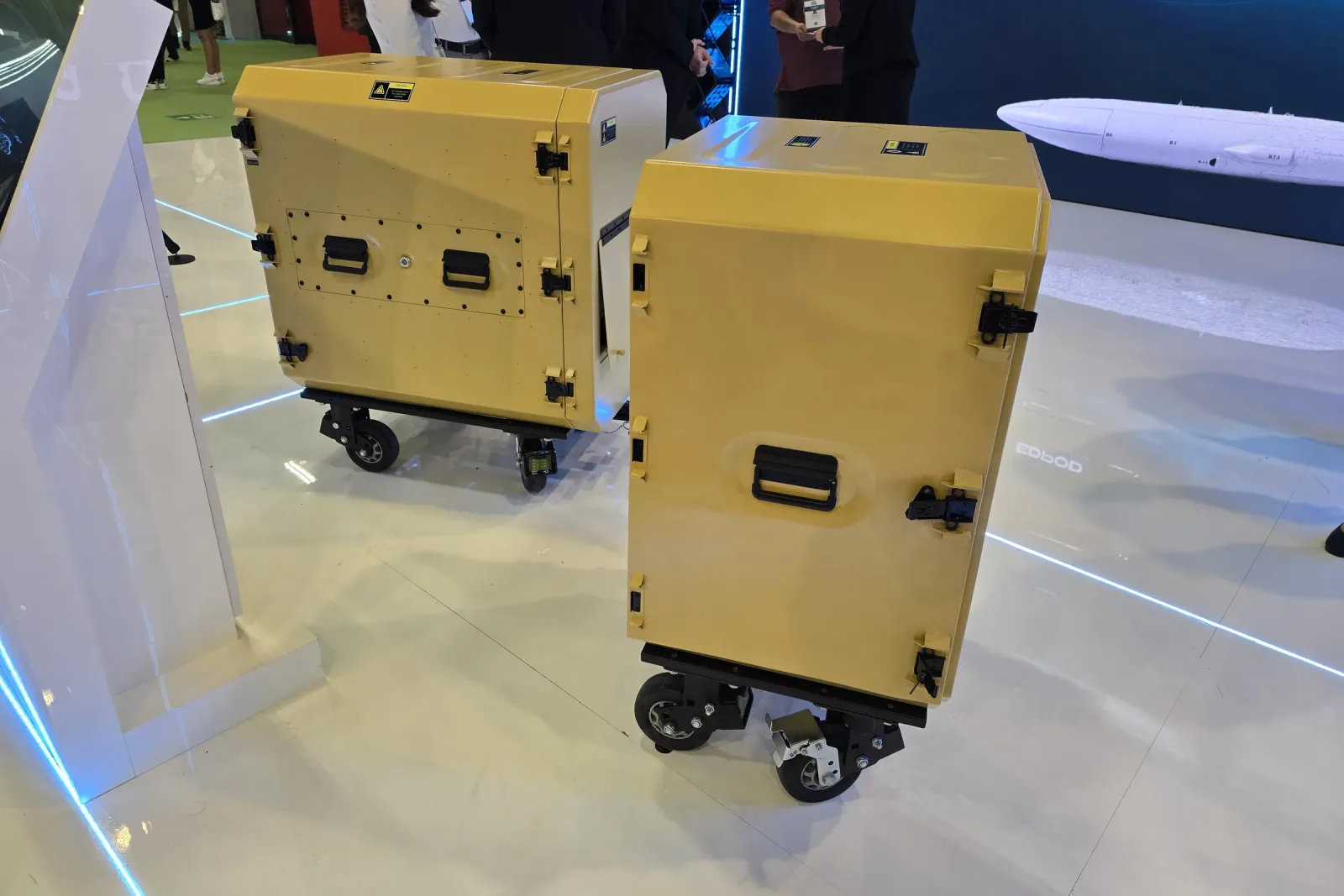 Two sand-coloured wheeled rack cabins standing closed side by side on the exhibition stand floor.