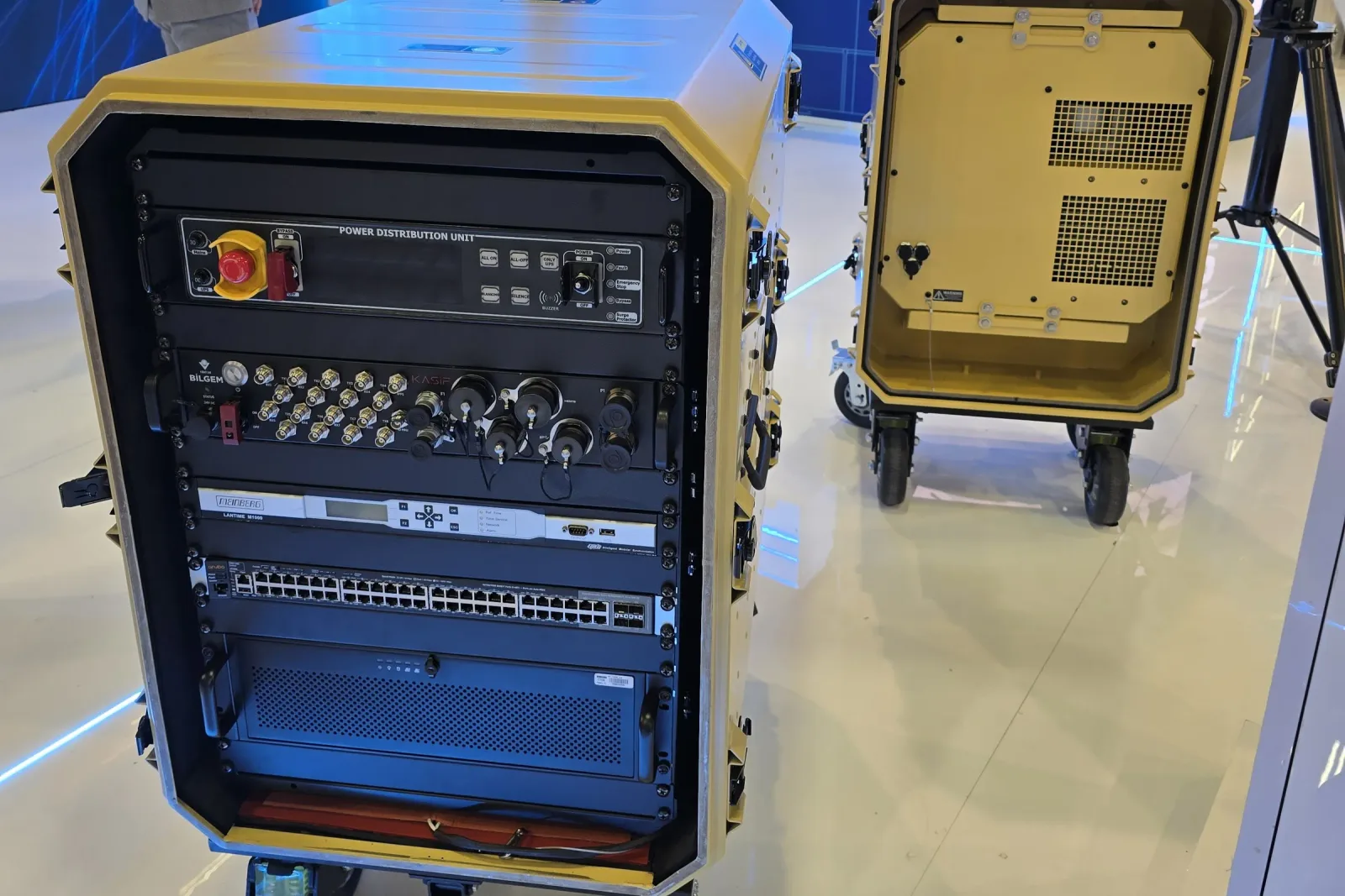 A rack cabin with its door removed, showing the 19-inch rack fitted with patch panels, a switch, a connector panel and an emergency stop button.