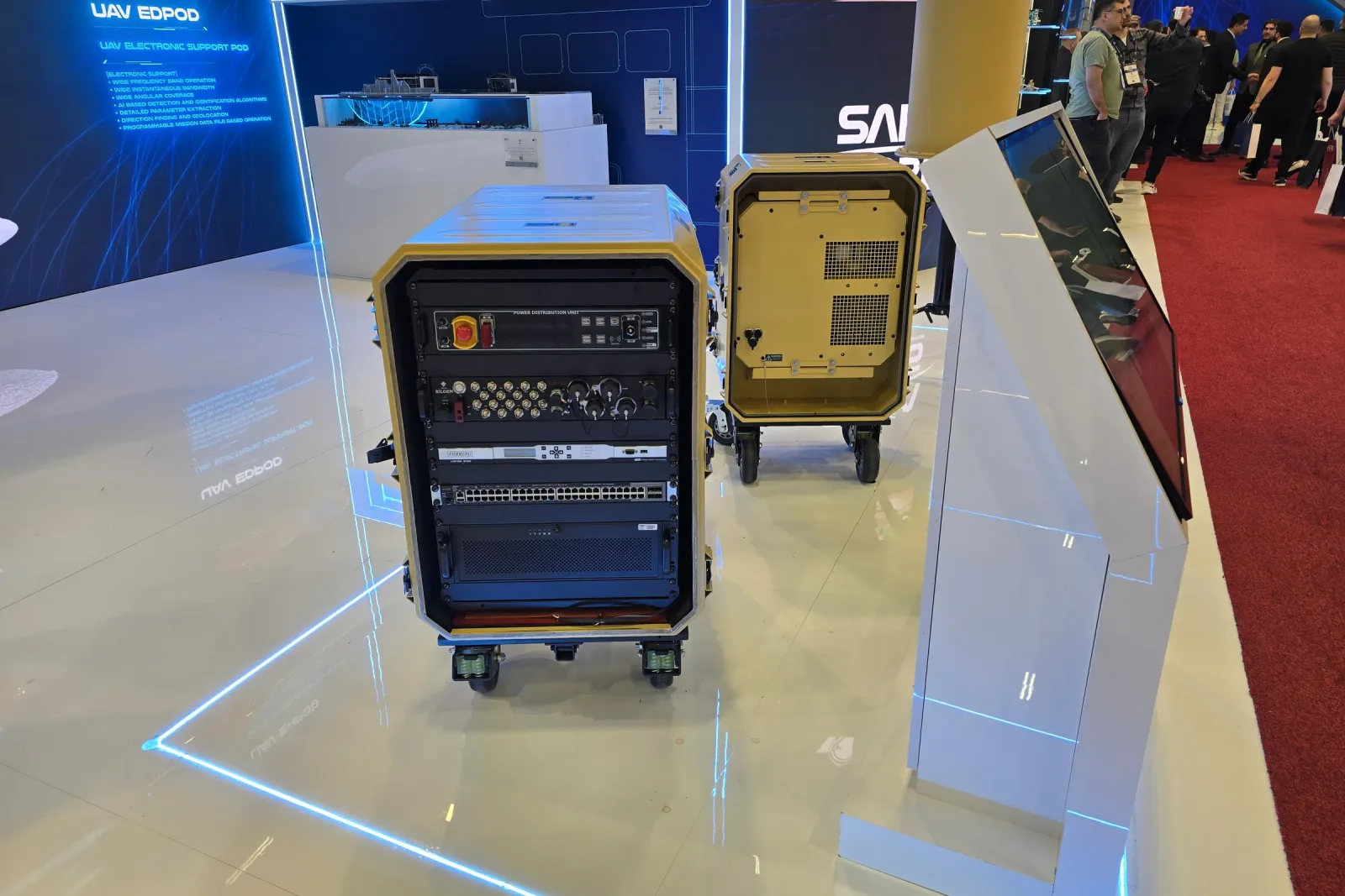 Two rack cabins on the stand, the open one showing its rack fit-out, with display screens behind them.