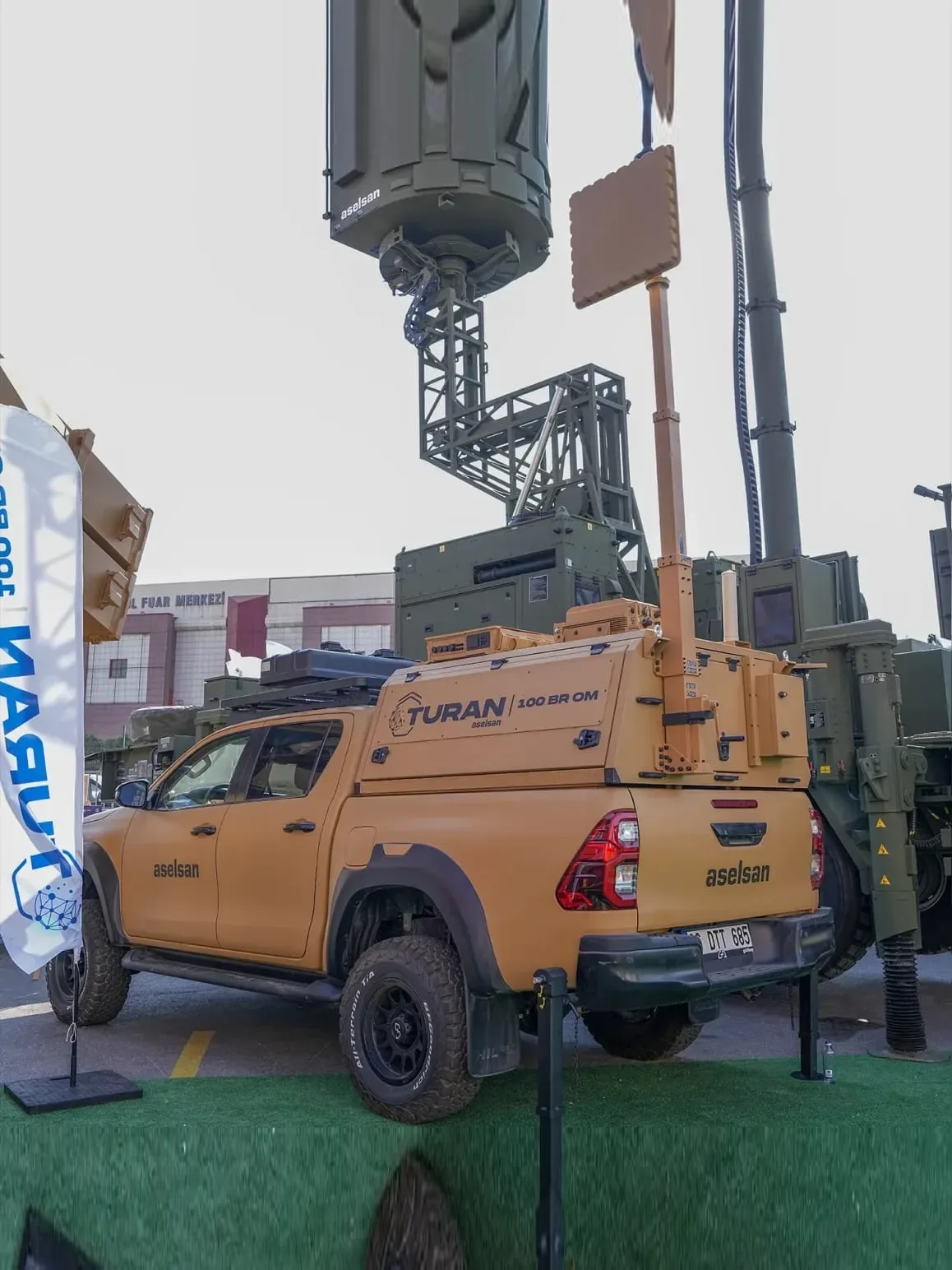 A telescopic mast raised from the bed of a pickup on the outdoor display area, carrying a payload at its head.