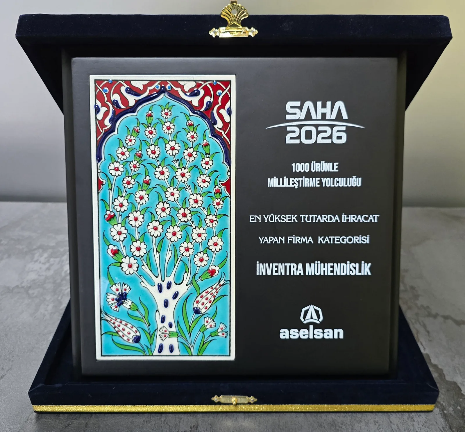 The plaque in its open presentation case: a hand-painted Iznik tile panel on the left, and engraved text on the right reading SAHA 2026, the localisation programme name, the award category and Inventra Mühendislik, above the ASELSAN logo.