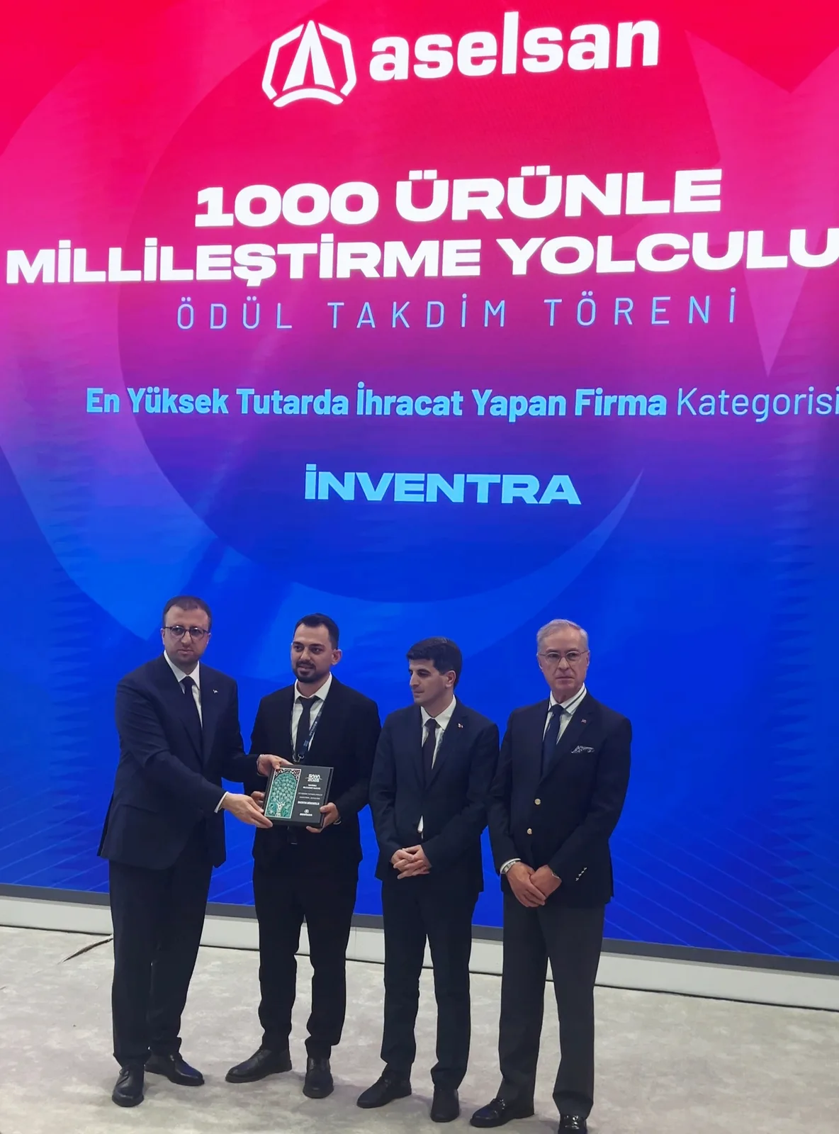 The award presentation at ASELSAN’s stand: four people, one holding the plaque, in front of a screen reading “1000 Ürünle Millileştirme Yolculuğu — Ödül Takdim Töreni — En Yüksek Tutarda İhracat Yapan Firma Kategorisi — İnventra”.