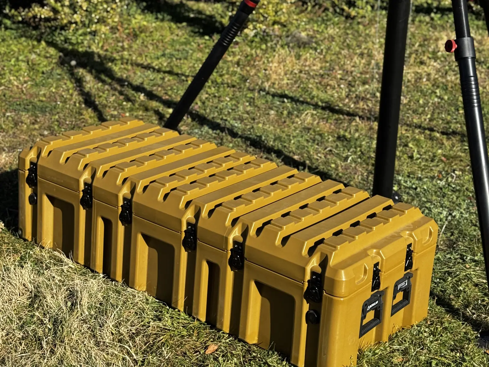 Yellow transport case on grass with the deployed tripod legs behind — scale and portability