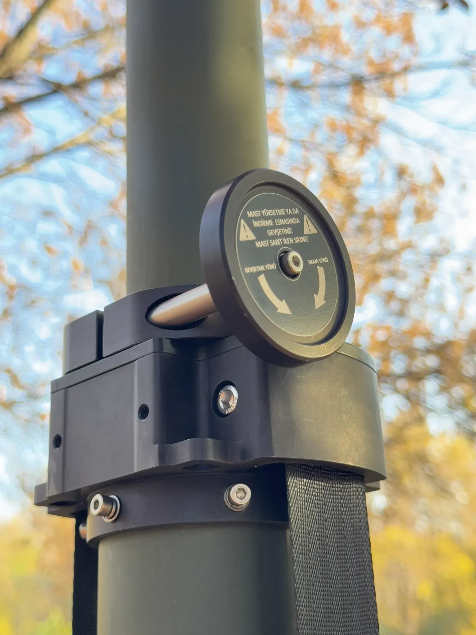 Rotating locking dial on the mast collar with strap, shot upward against sky and yellow leaves.