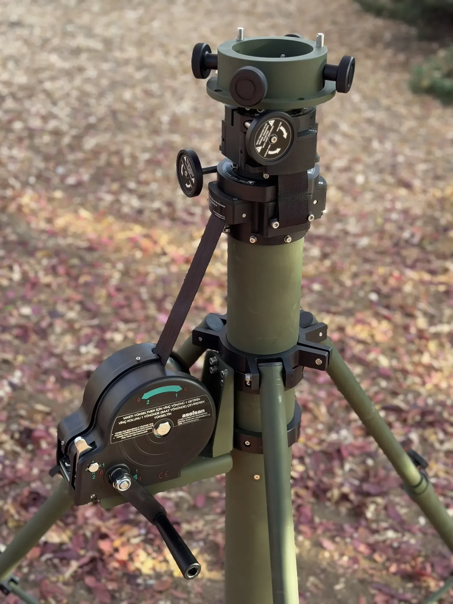Mast head, rotator and winch with crank handle fitted, tripod standing on a gravel path.