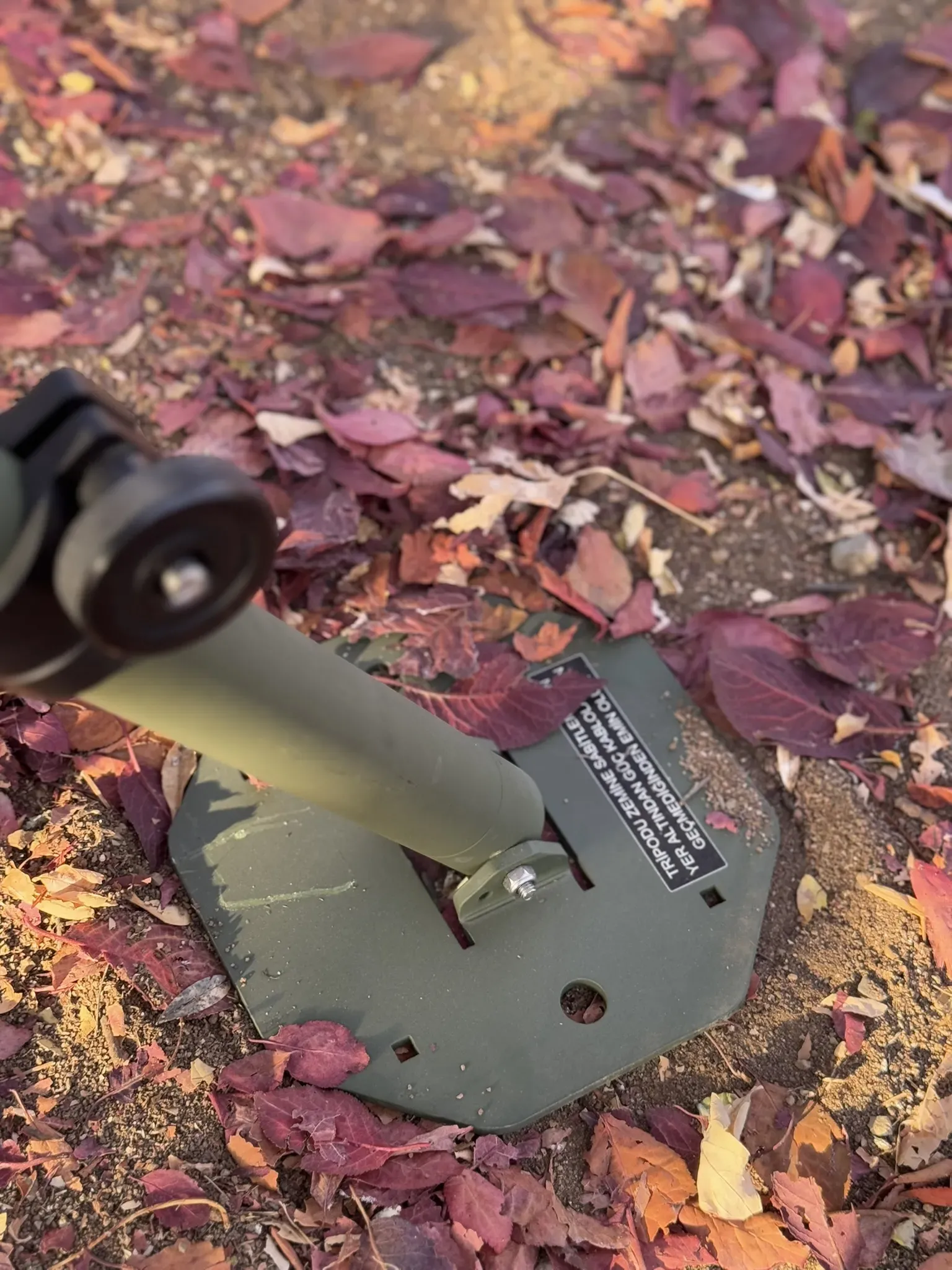 Tripod leg foot bolted to its olive octagonal plate lying on red and brown leaves.