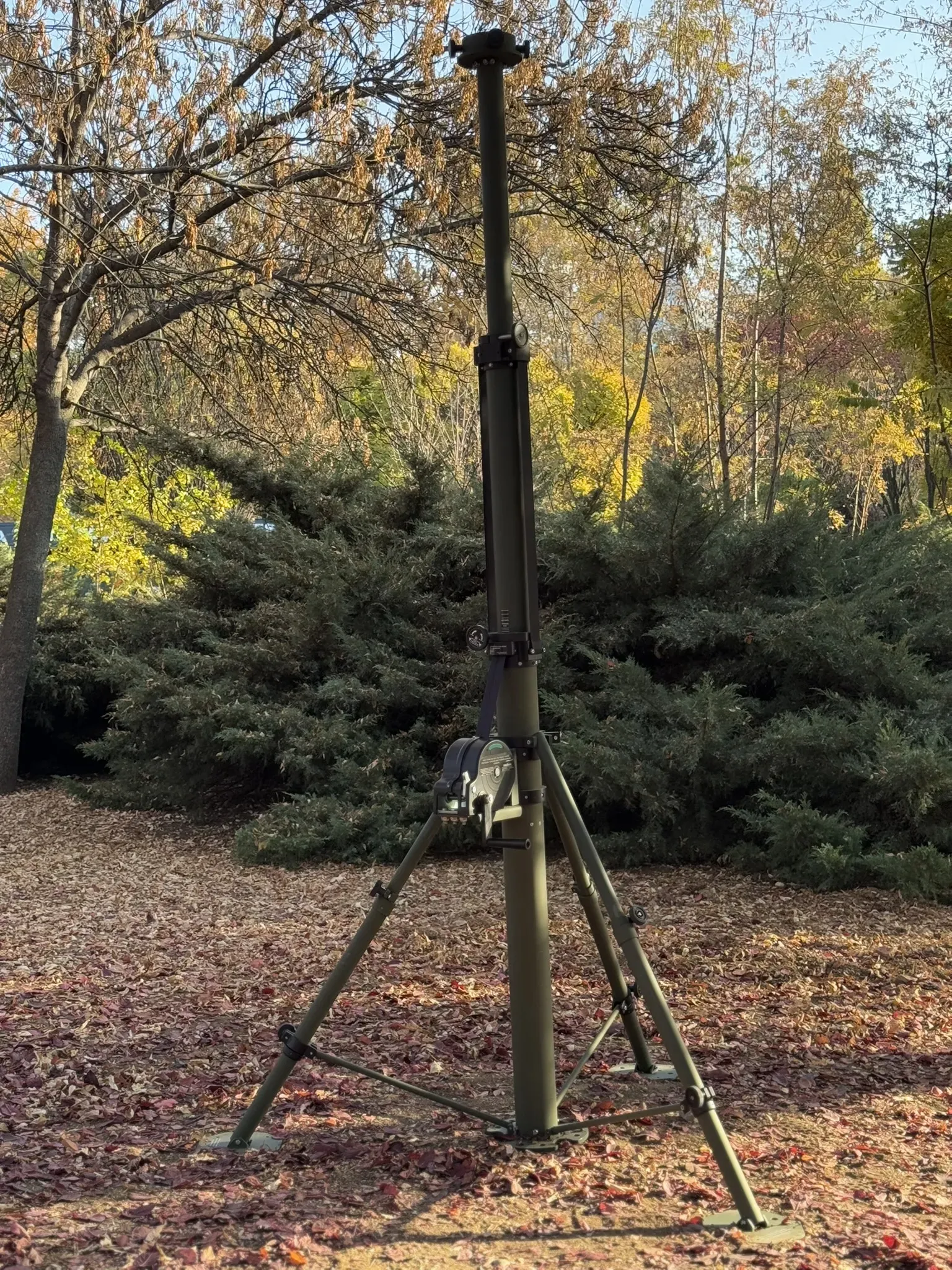 Mast fully extended to full height on its tripod in woodland, autumn trees behind.
