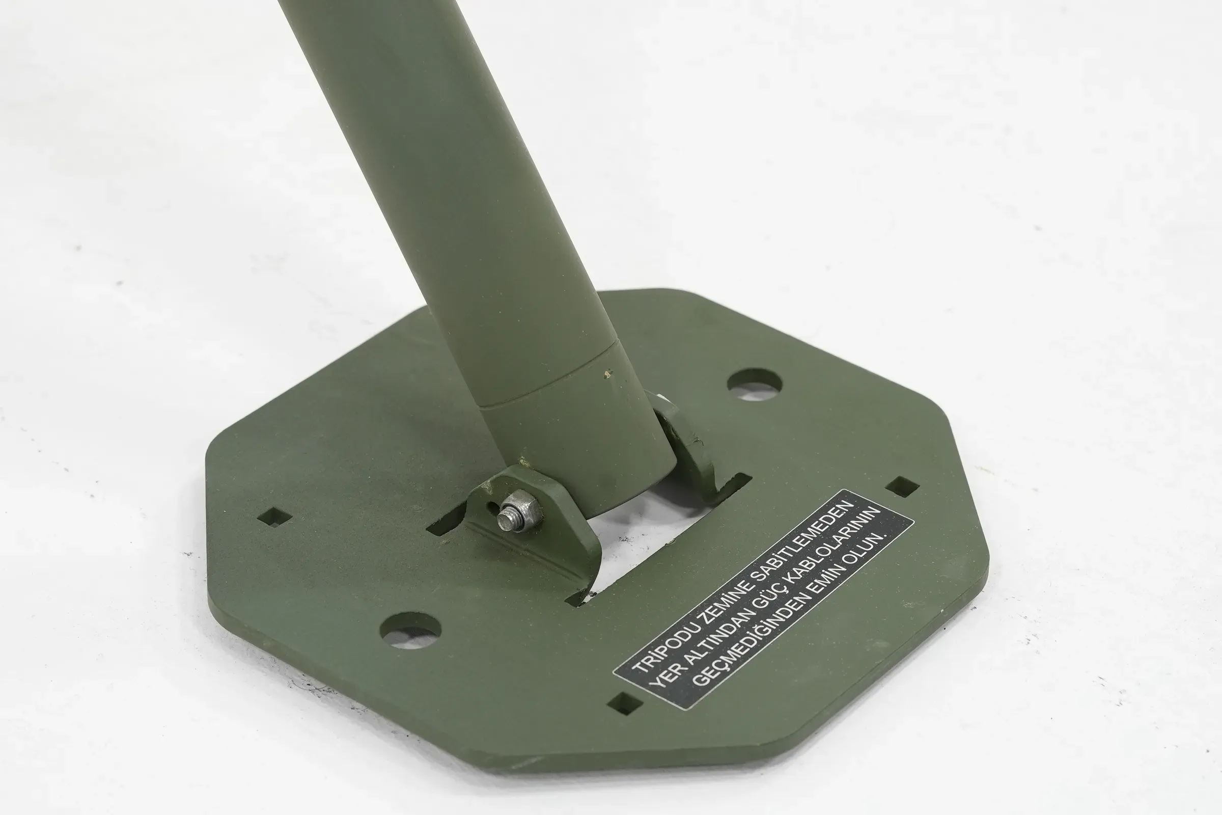 Angled foot detail showing the mast tube bolted to an octagonal olive green base plate with warning label.