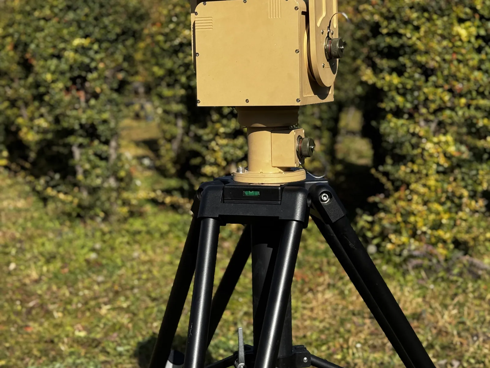 With the full tripod against a green fence and open sky — scale and field setup