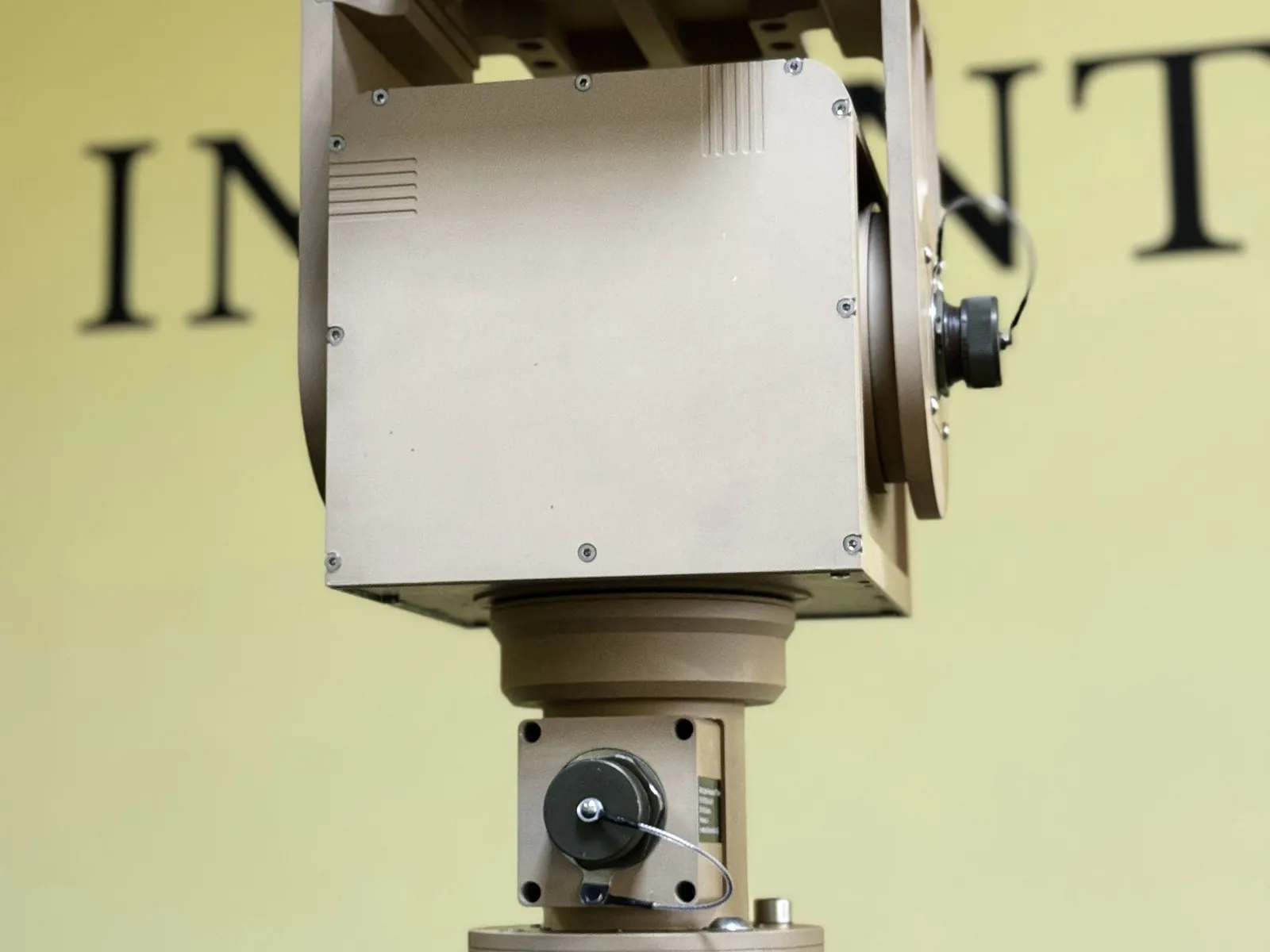 Tan unit head on against a plain wall: the wide sun shade plate and the long azimuth column