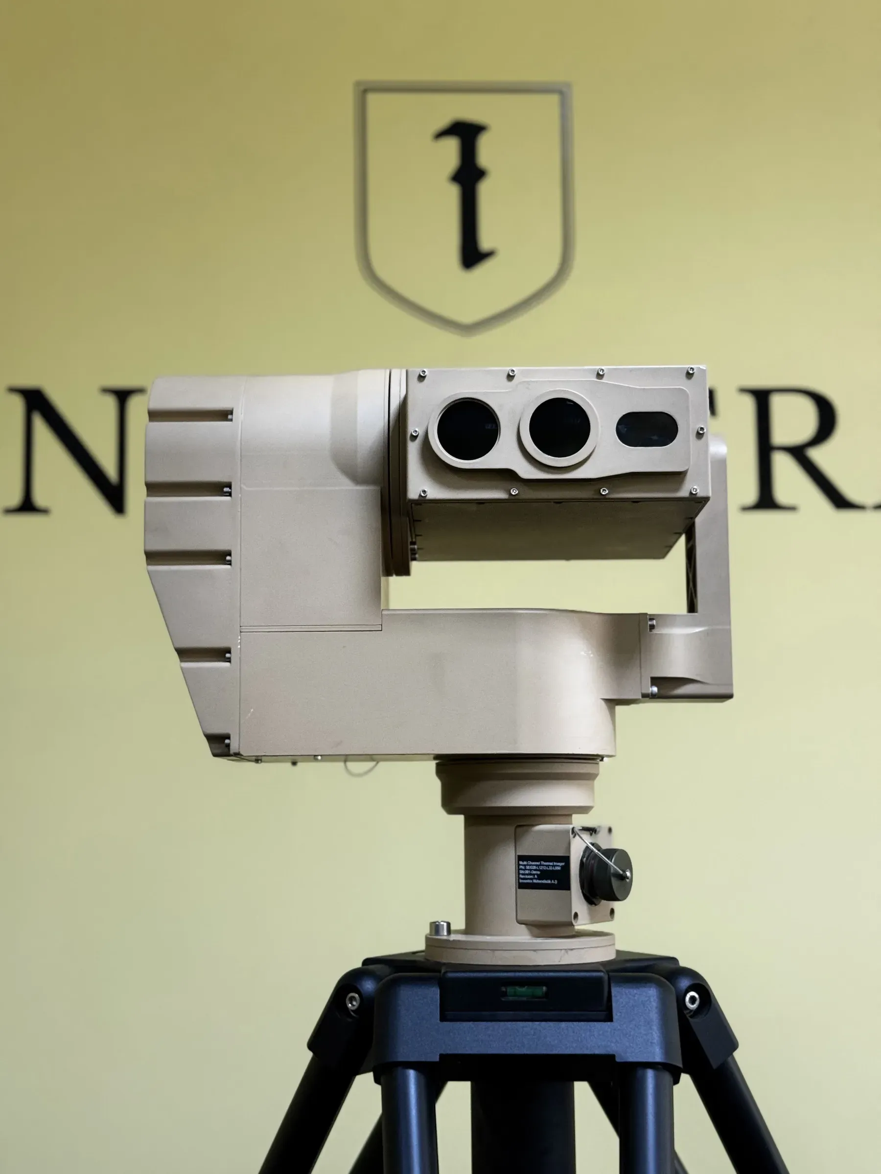 Grey positioner carrying a triple-aperture thermal imager head on a tripod, front view indoors.