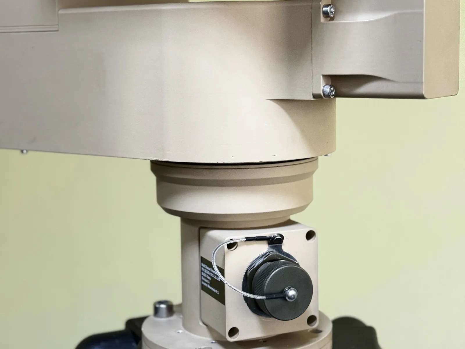 Close view of the connection panel: circular military connector with a tethered cover, identification plate and mounting flange