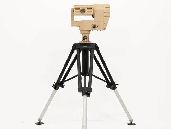 Distant full studio view of the tan sensor head and positioner on an extended black tripod, front angle.