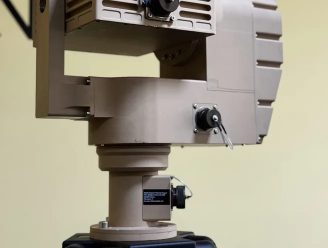 Tan PED12 with SEB20 payload on a tripod seen from the rear left, cable tail hanging from the drive housing.