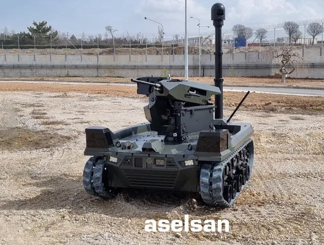 Tracked UGV carrying a mast-mounted gimbal on gravel ground, ASELSAN watermark across the frame.