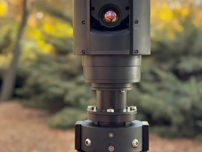 Close outdoor view of the SEG10 gimbal head and mast top section, autumn trees blurred behind.