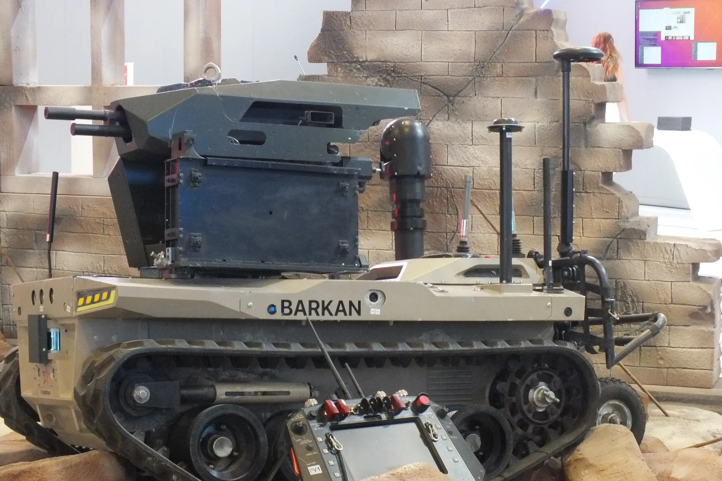 Tan tracked BARKAN unmanned ground vehicle on a rock diorama, telescopic mast extended vertically behind its remote weapon station.