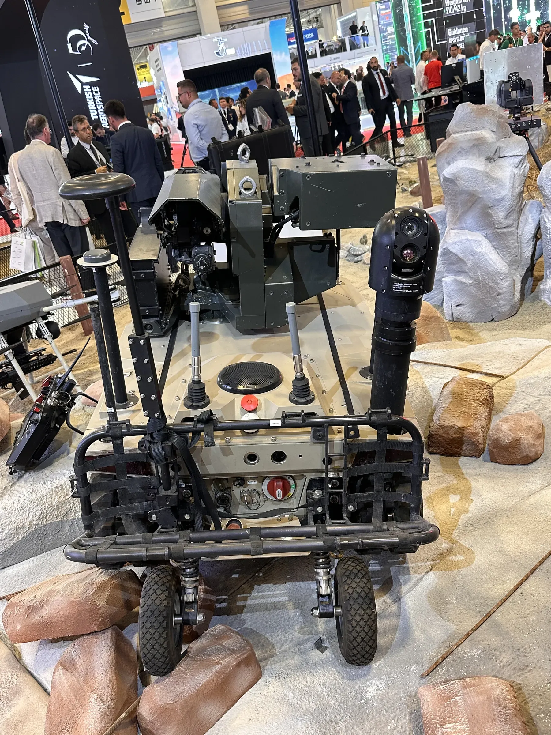 Front view of wheeled-tracked robot on a rock set with mast and sensor payload raised, visitors gathered behind.
