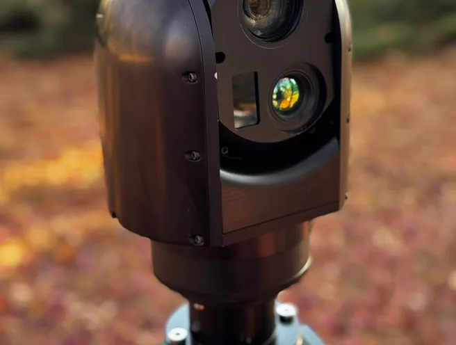 Close outdoor view of the SEG12 gimbal head with sunlit lens coatings above the mast joint.