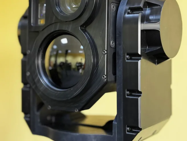SEG14 gimbal photographed from slightly below in its yoke, main optics facing the camera.