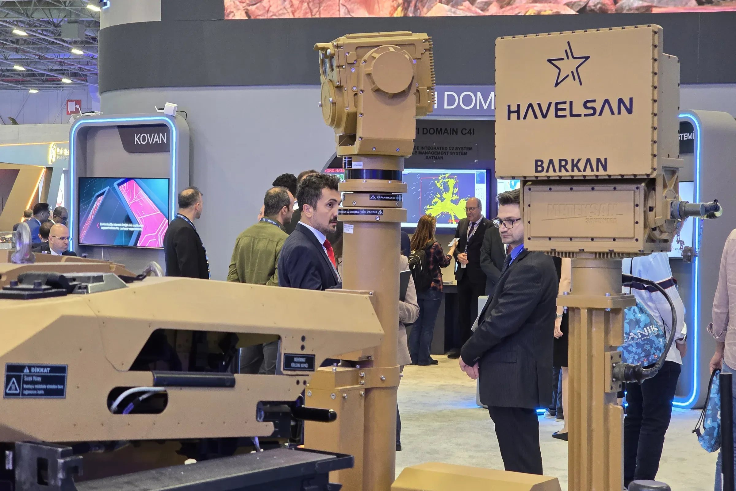 Extended MEM10 mast with SEG14 sensor head rising above the UGV hull, HAVELSAN BARKAN sign and visitors behind.