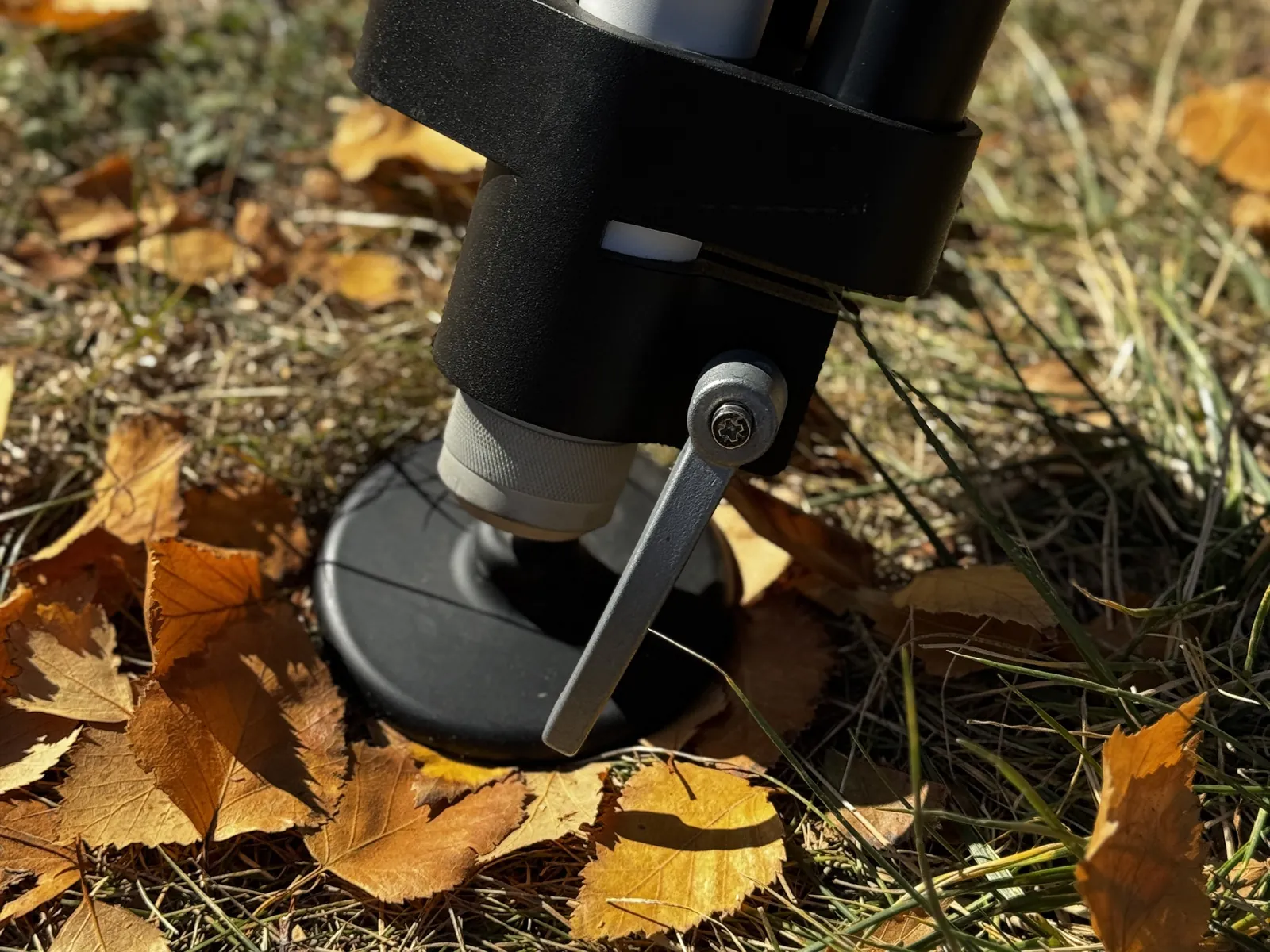Close view of a leg end, clamp lever and the wide pad foot on leaf-covered ground