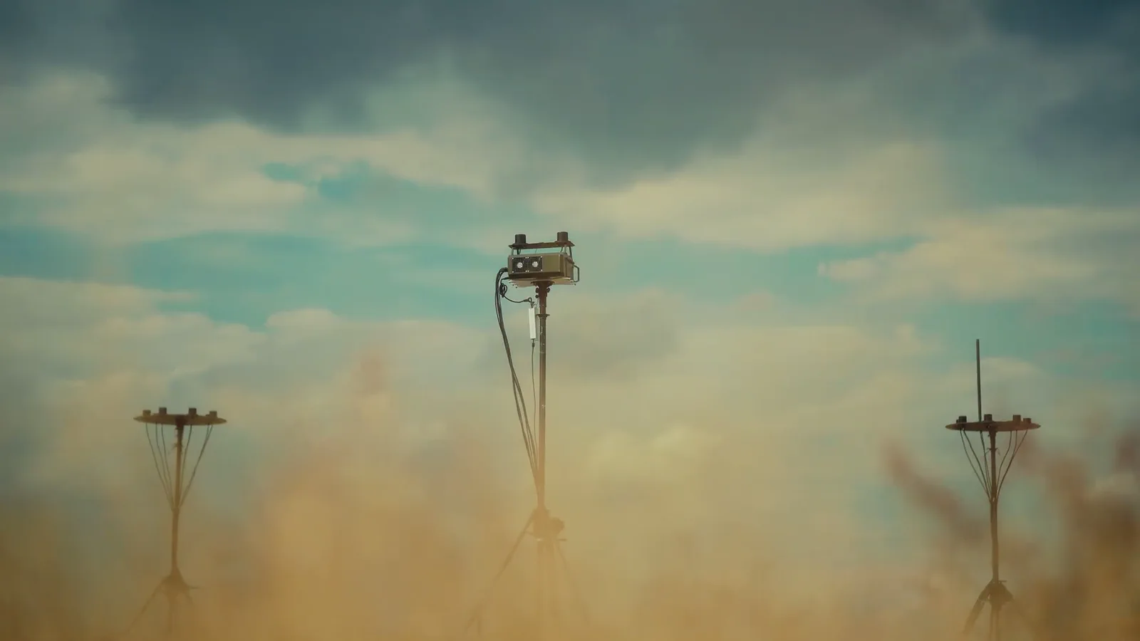 Three guyed masts stand in drifting dust, two carrying disc antenna arrays and the centre one a sensor head.