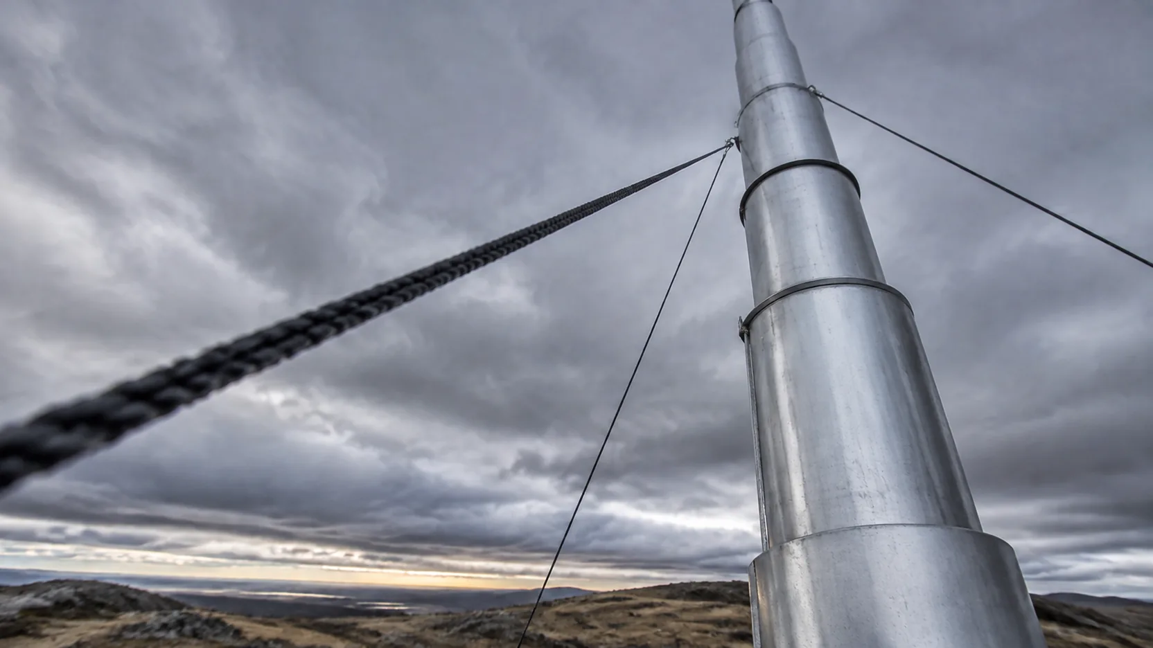 Looking up the length of a telescopic aluminium mast against fast-moving cloud, guy ropes running taut off-frame.
