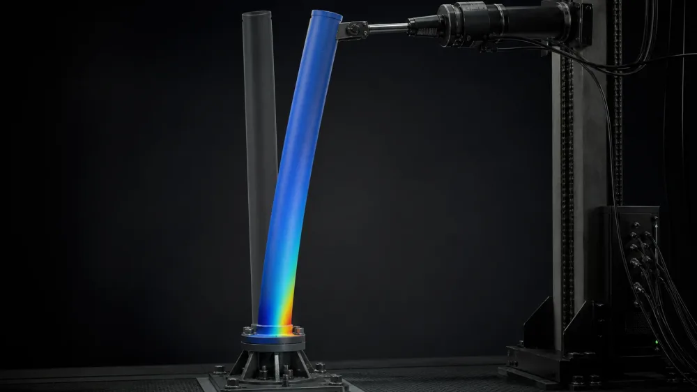 A tubular specimen bent under a lateral actuator load beside its straight reference, the stress field concentrating at the bolted base flange.