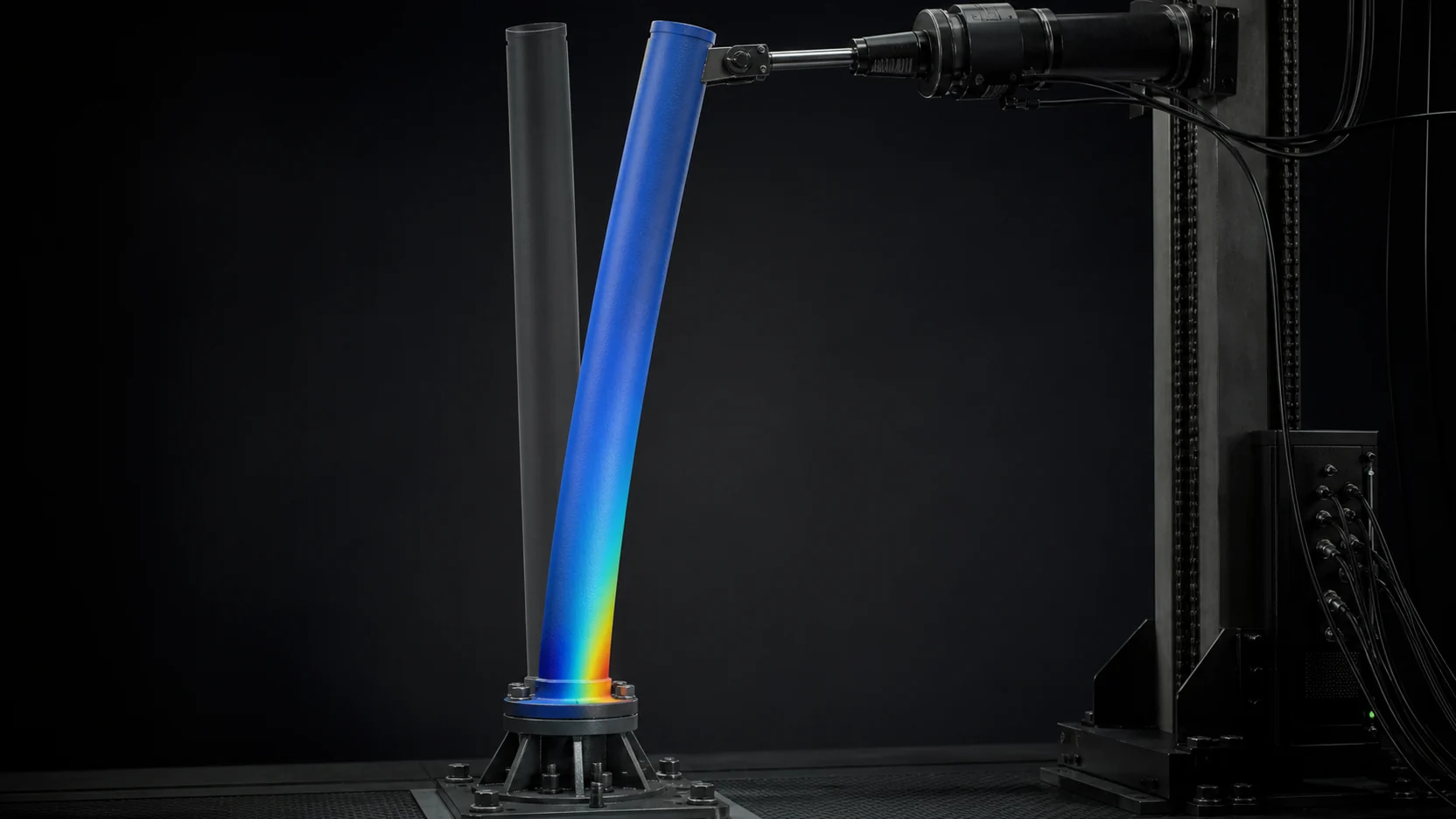 A tubular specimen bent under a lateral actuator load beside its straight reference, the stress field concentrating at the bolted base flange