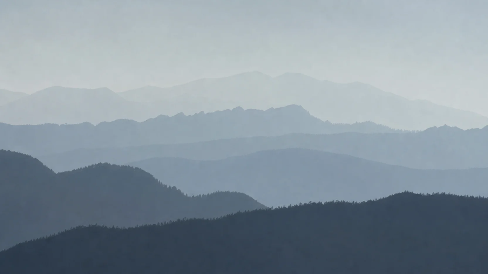 Forested ridgelines receding into dense cold morning haze, each line paler than the one before it