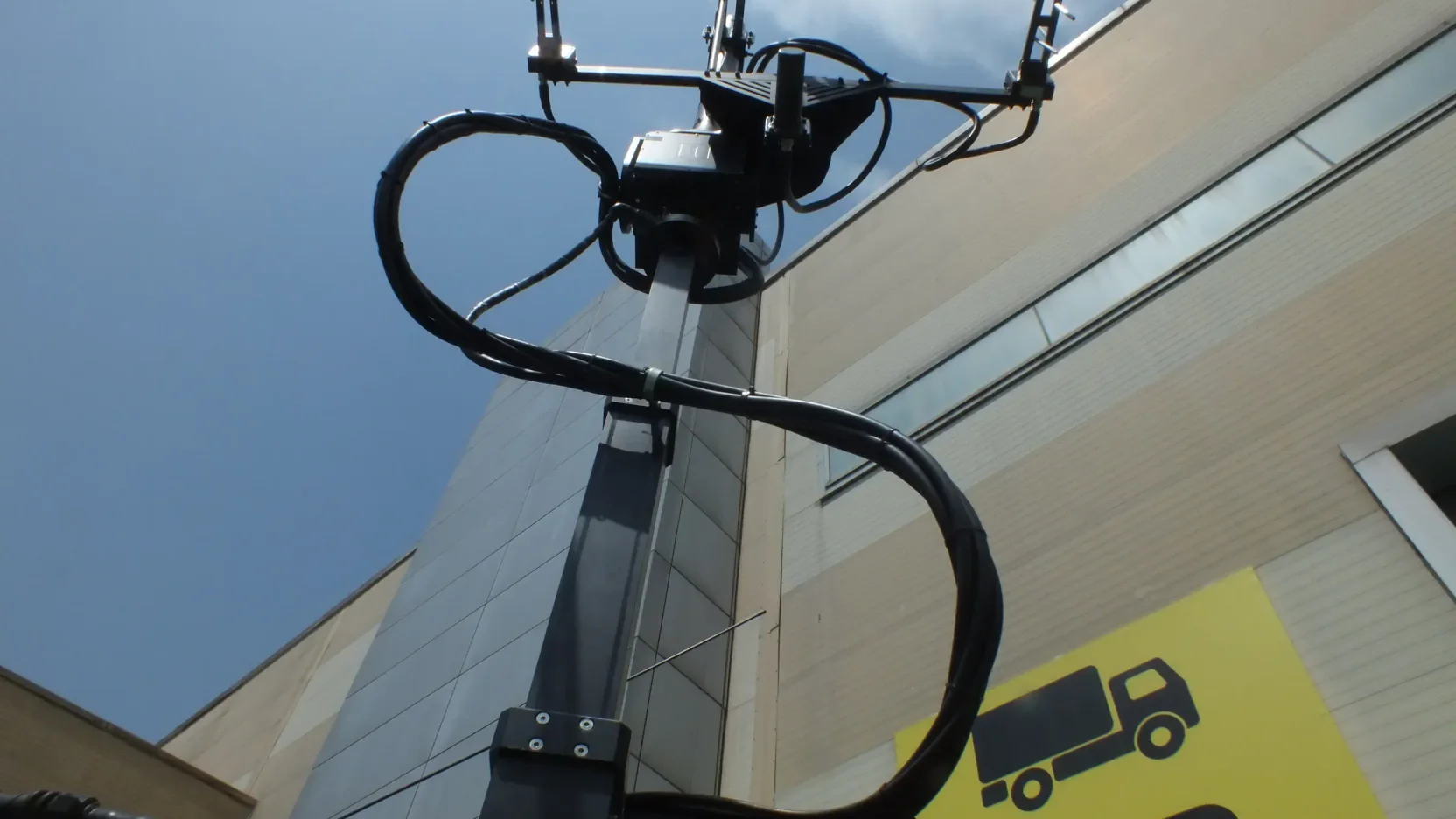 A mast-top antenna assembly seen from below, its service cable looped in a wide arc back down the mast.